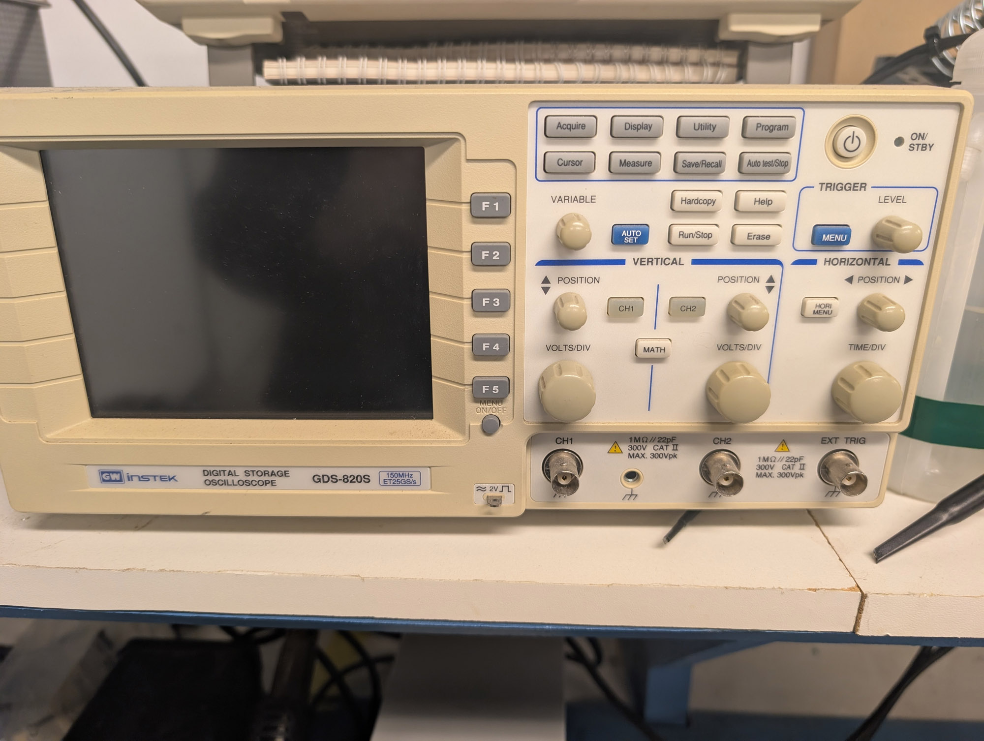 A beige LCD oscilloscope with two channels and a trigger input, as well as a small number of knobs and buttons to the right of the screen